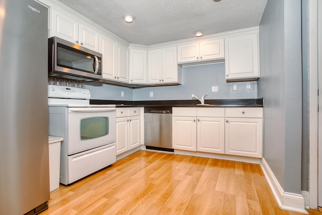 kitchen featuring appliances with stainless steel finishes, dark countertops, light wood-style flooring, and white cabinetry