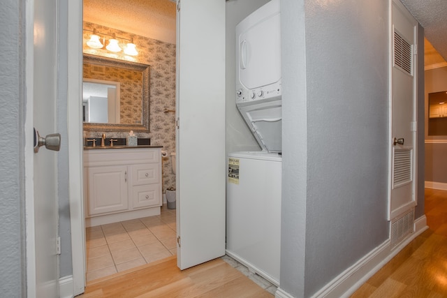 clothes washing area with stacked washer and dryer, a textured ceiling, light wood-type flooring, laundry area, and wallpapered walls