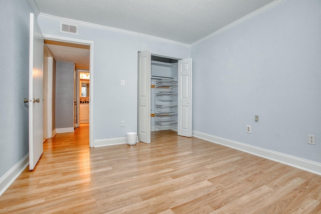 unfurnished bedroom featuring a textured ceiling, ornamental molding, and light wood-style flooring