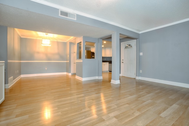 empty room with a textured ceiling, visible vents, baseboards, ornamental molding, and light wood-type flooring