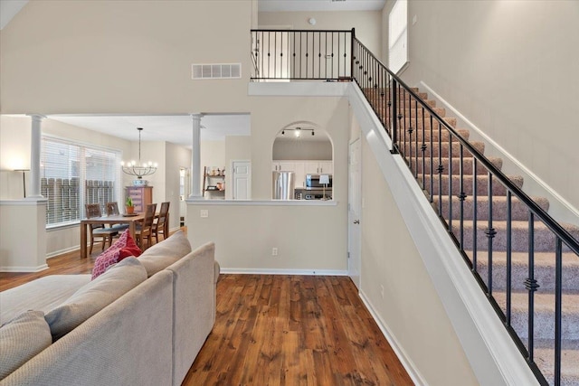 staircase with a towering ceiling, decorative columns, visible vents, and wood finished floors