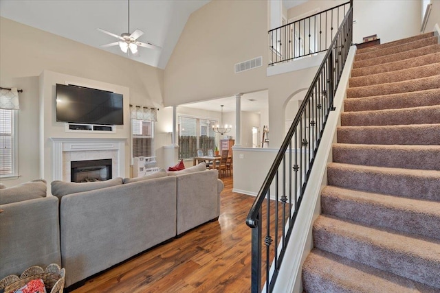 living room featuring high vaulted ceiling, a fireplace, wood finished floors, visible vents, and stairway