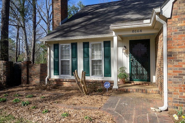 property entrance with brick siding, a chimney, and a shingled roof