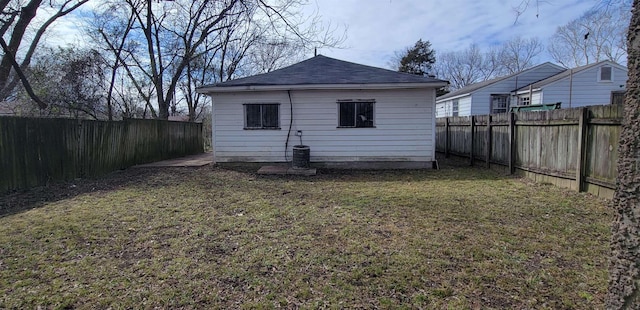 back of property with a shingled roof, a lawn, an outdoor structure, and a fenced backyard