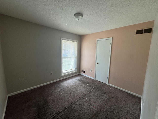 spare room with a textured ceiling, carpet flooring, visible vents, and baseboards