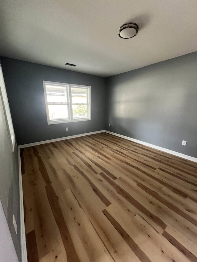 spare room featuring baseboards, visible vents, and wood finished floors