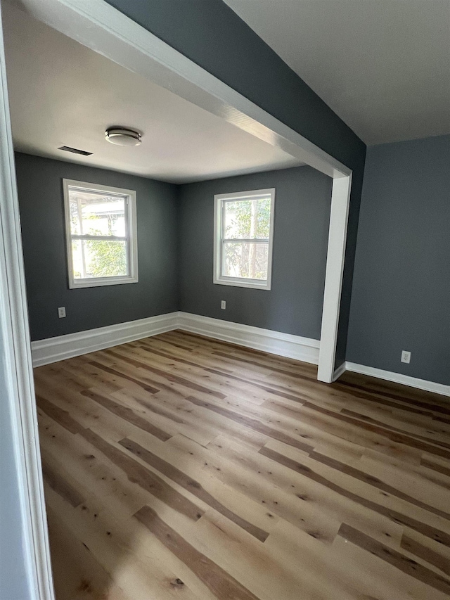 empty room featuring a healthy amount of sunlight, visible vents, baseboards, and wood finished floors