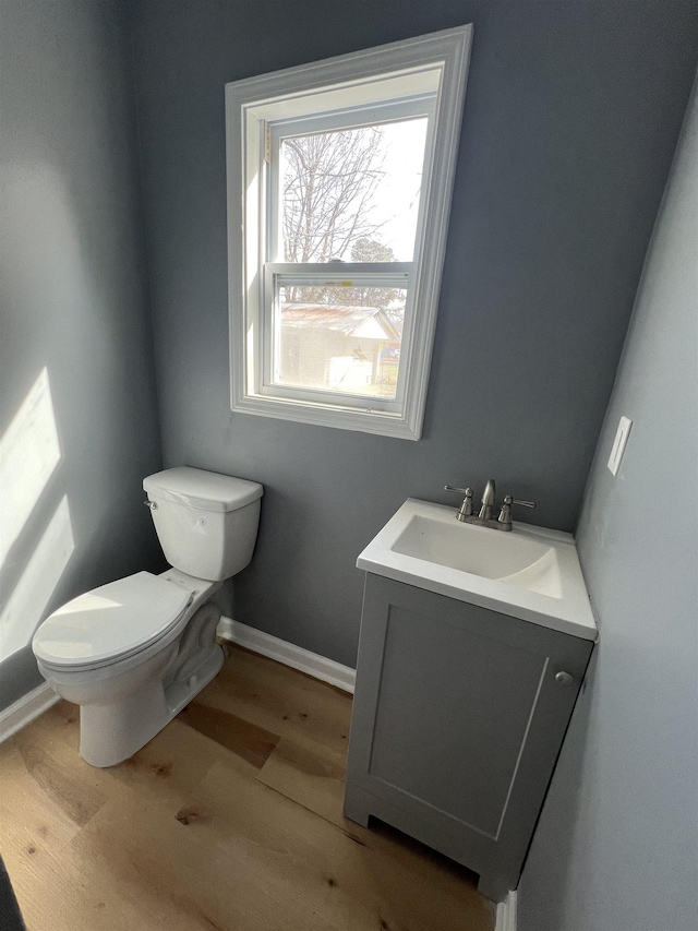 half bath with baseboards, vanity, toilet, and wood finished floors