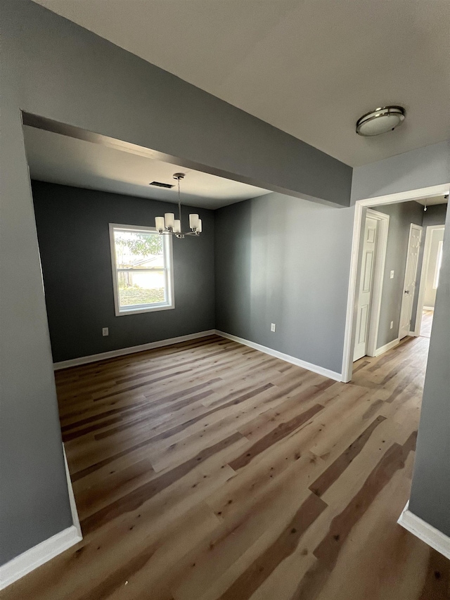 unfurnished dining area with baseboards, wood finished floors, and a notable chandelier