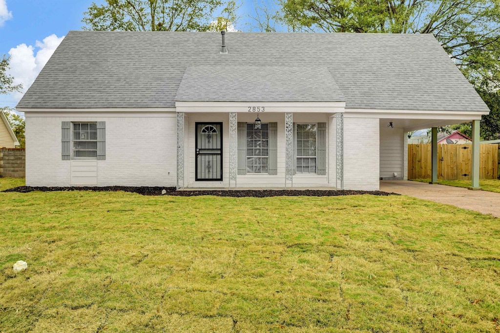 view of front of home with brick siding, concrete driveway, fence, an attached carport, and a front lawn