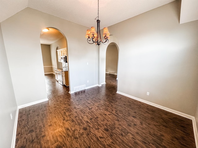 empty room with arched walkways, dark wood-style flooring, visible vents, and an inviting chandelier