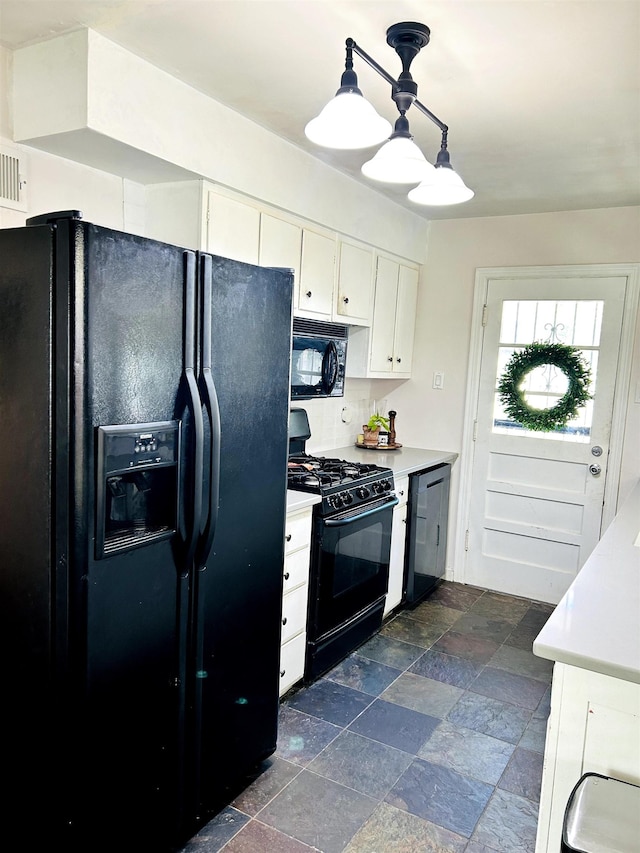 kitchen featuring decorative light fixtures, light countertops, white cabinets, stone finish floor, and black appliances