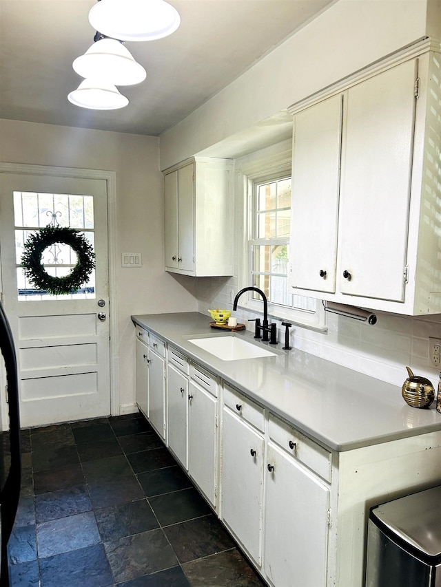 kitchen featuring white cabinets, light countertops, stone finish floor, and a sink