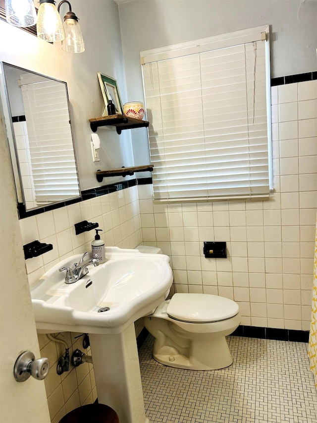 bathroom with tile patterned flooring, tile walls, toilet, and a sink