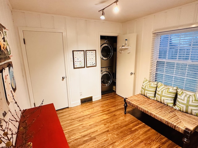 sitting room featuring visible vents, light wood finished floors, rail lighting, a decorative wall, and stacked washer / drying machine