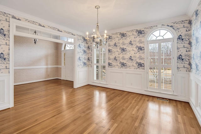 unfurnished dining area with a wainscoted wall, wallpapered walls, and light wood-type flooring