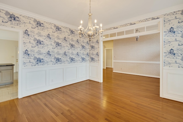 unfurnished dining area featuring light wood finished floors, a wainscoted wall, wallpapered walls, and ornamental molding