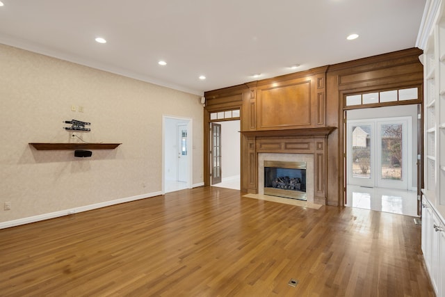 unfurnished living room featuring a fireplace, crown molding, wood finished floors, and baseboards