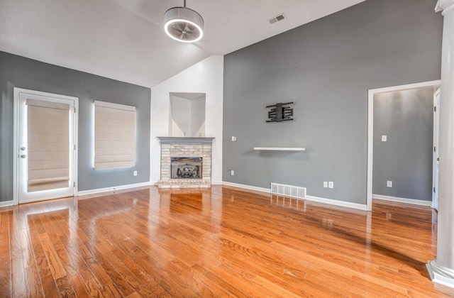 unfurnished living room featuring lofted ceiling, a brick fireplace, wood finished floors, and visible vents