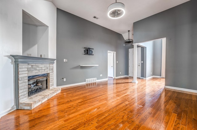 unfurnished living room featuring visible vents, wood finished floors, a fireplace, and ornate columns