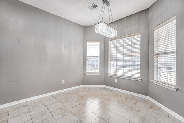 empty room with a textured ceiling, a healthy amount of sunlight, visible vents, and baseboards