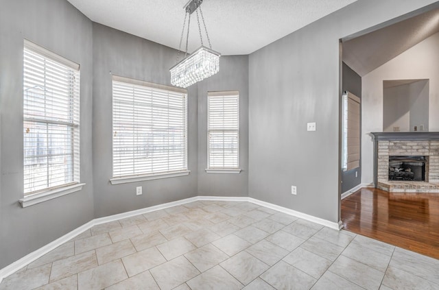 unfurnished dining area with a brick fireplace, baseboards, a chandelier, tile patterned floors, and a textured ceiling