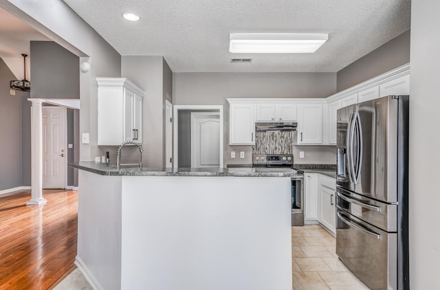 kitchen featuring under cabinet range hood, stainless steel appliances, a peninsula, and decorative columns