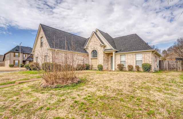 french country home with a front yard, fence, brick siding, and a shingled roof