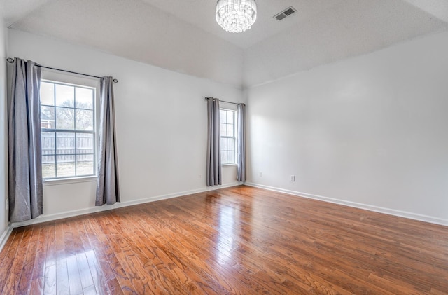 empty room with visible vents, baseboards, an inviting chandelier, and hardwood / wood-style flooring