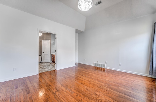 unfurnished room featuring hardwood / wood-style flooring, baseboards, visible vents, and a chandelier