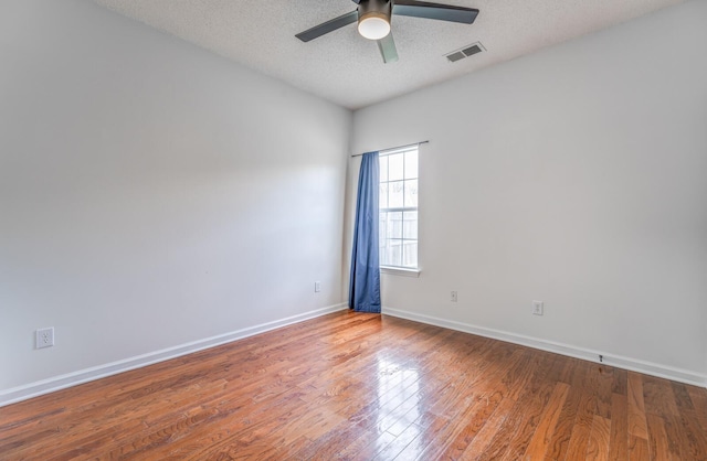 spare room with visible vents, a ceiling fan, a textured ceiling, wood finished floors, and baseboards