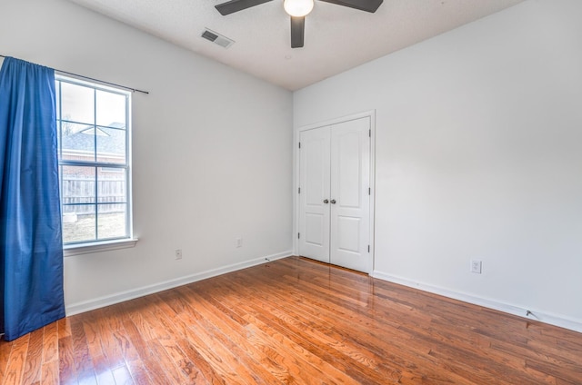 empty room with ceiling fan, wood finished floors, visible vents, and baseboards