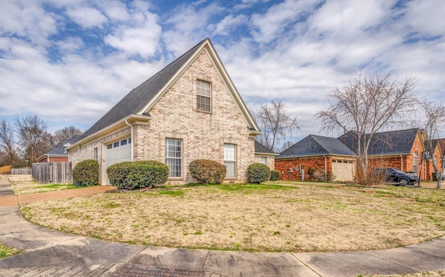 view of side of property featuring brick siding, a lawn, an attached garage, and fence