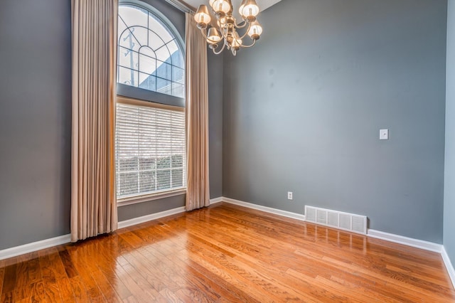 spare room with an inviting chandelier, baseboards, visible vents, and wood-type flooring