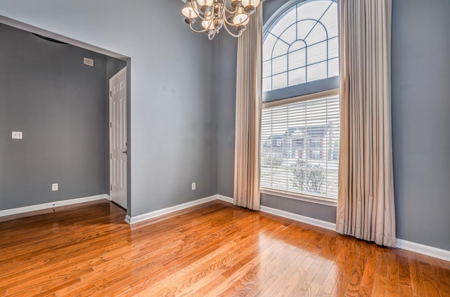 unfurnished room featuring a notable chandelier, baseboards, and hardwood / wood-style flooring