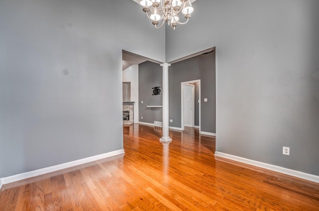 spare room featuring baseboards, ornate columns, a high ceiling, light wood-style flooring, and a fireplace