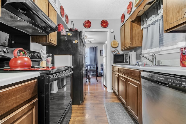 kitchen featuring range hood, light wood-style flooring, a sink, black appliances, and light countertops