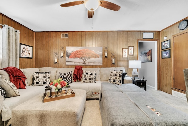 living area featuring a ceiling fan, baseboards, visible vents, carpet floors, and wood walls