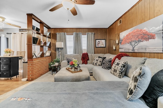 living room with visible vents, ceiling fan, light wood-style floors, and wooden walls