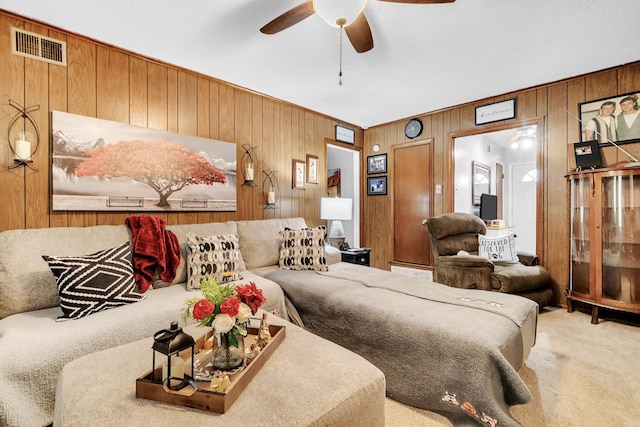 carpeted bedroom with wooden walls, a ceiling fan, and visible vents