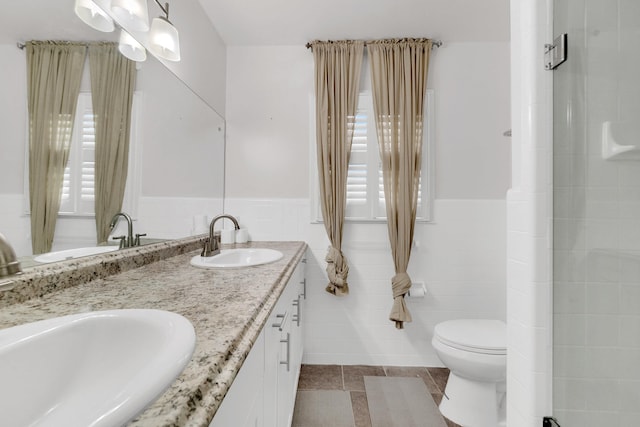 bathroom with double vanity, a sink, wainscoting, tile walls, and toilet