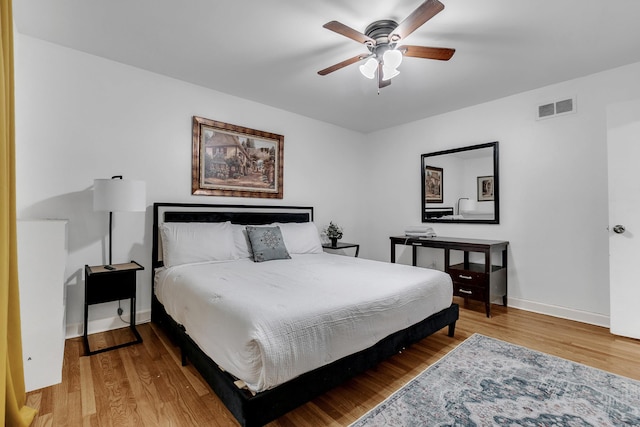 bedroom with ceiling fan, visible vents, baseboards, and wood finished floors