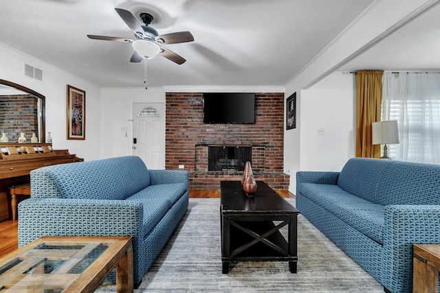 living area featuring wood finished floors, visible vents, brick wall, a fireplace, and crown molding