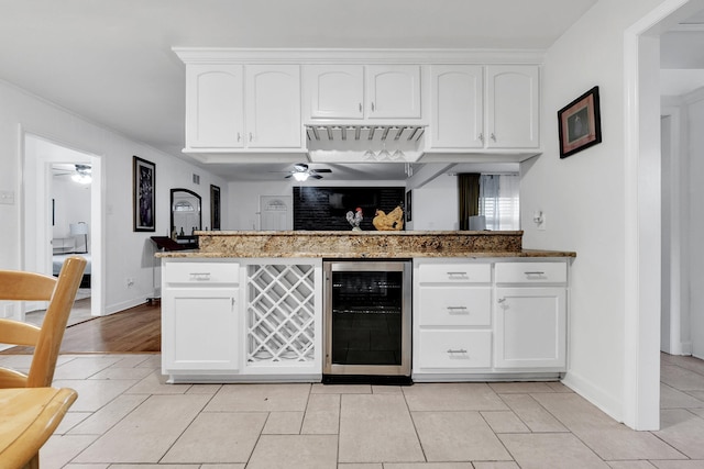 kitchen featuring a ceiling fan, white cabinets, beverage cooler, and stone countertops