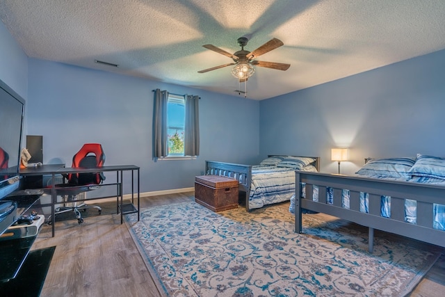bedroom with visible vents, a textured ceiling, baseboards, and wood finished floors