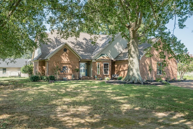 view of front facade featuring brick siding, roof with shingles, and a front yard