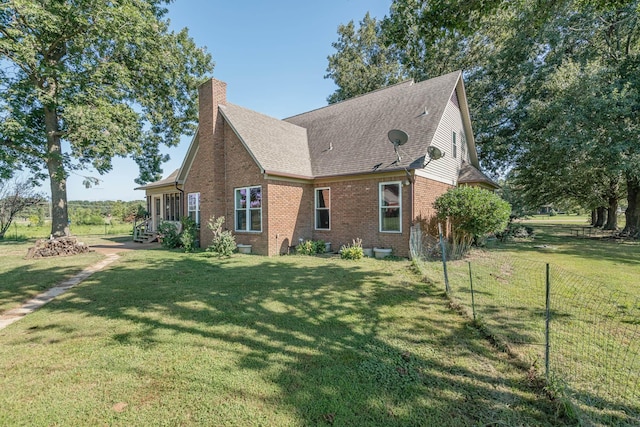 view of property exterior with a lawn, fence, a shingled roof, brick siding, and a chimney