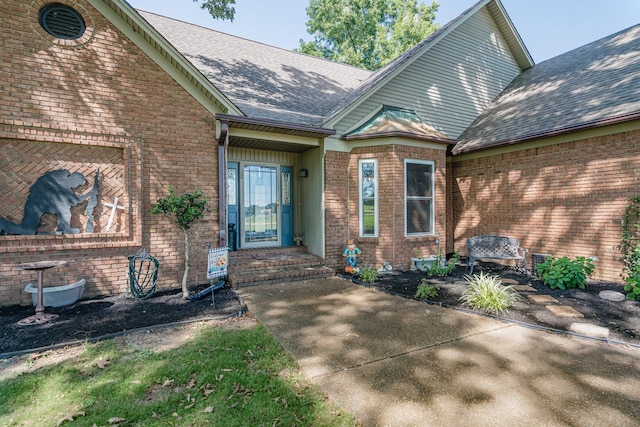 view of exterior entry featuring brick siding and roof with shingles