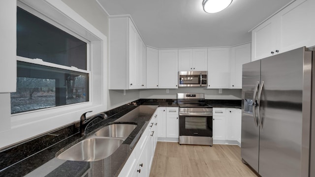 kitchen with dark stone counters, light wood-style flooring, a sink, stainless steel appliances, and white cabinets