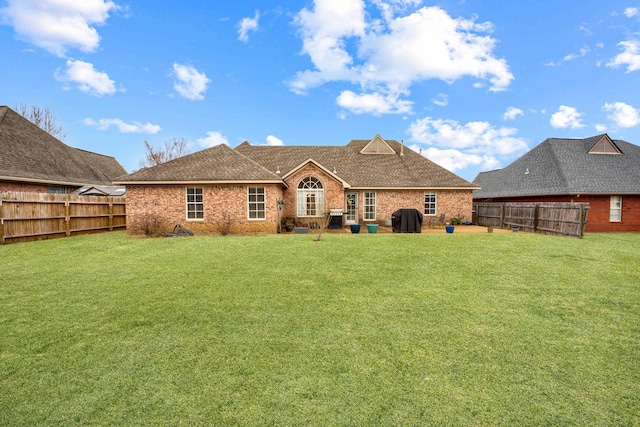 rear view of house featuring a yard, brick siding, roof with shingles, and a fenced backyard